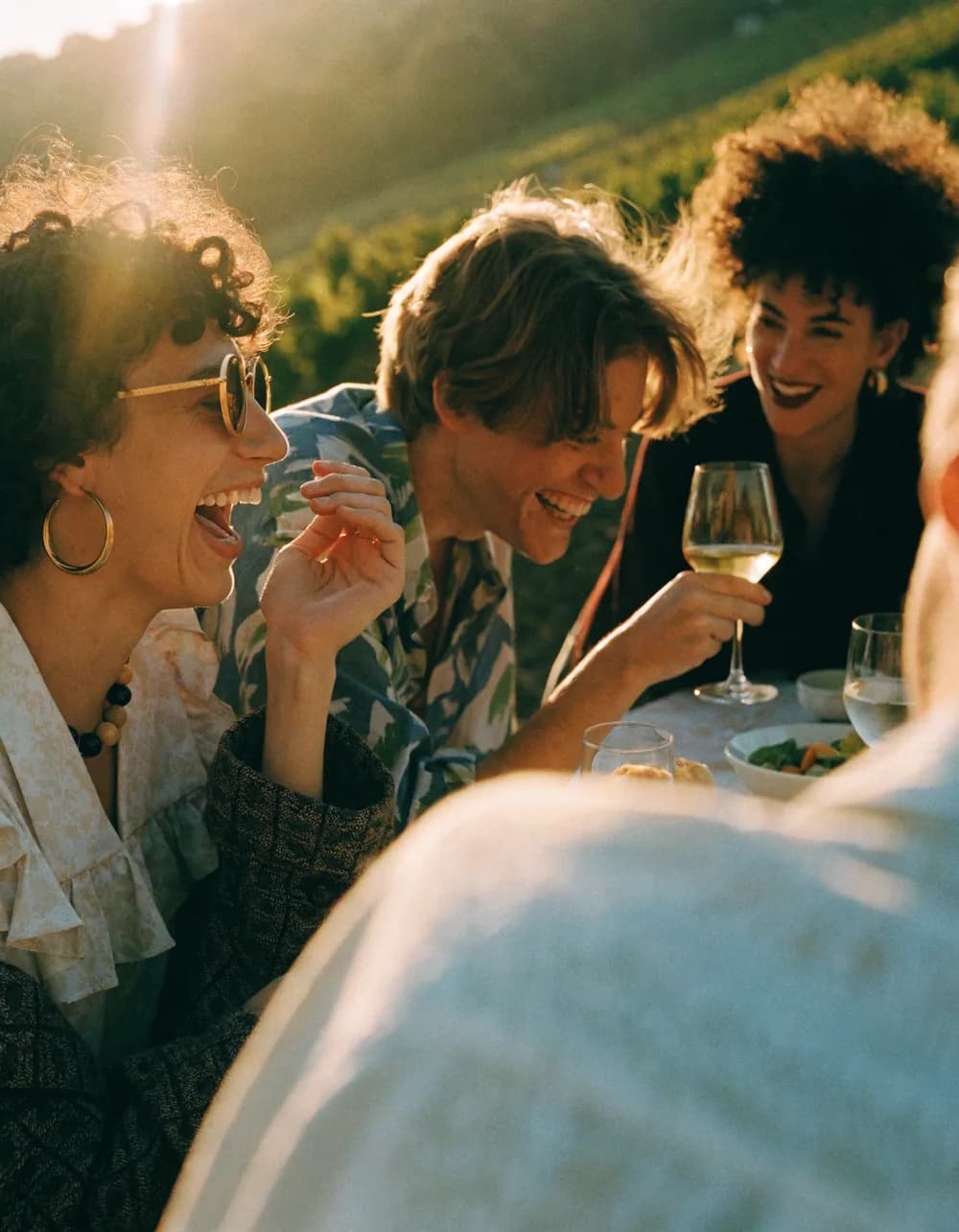 A candid golden-hour moment of people laughing at a vineyard table.