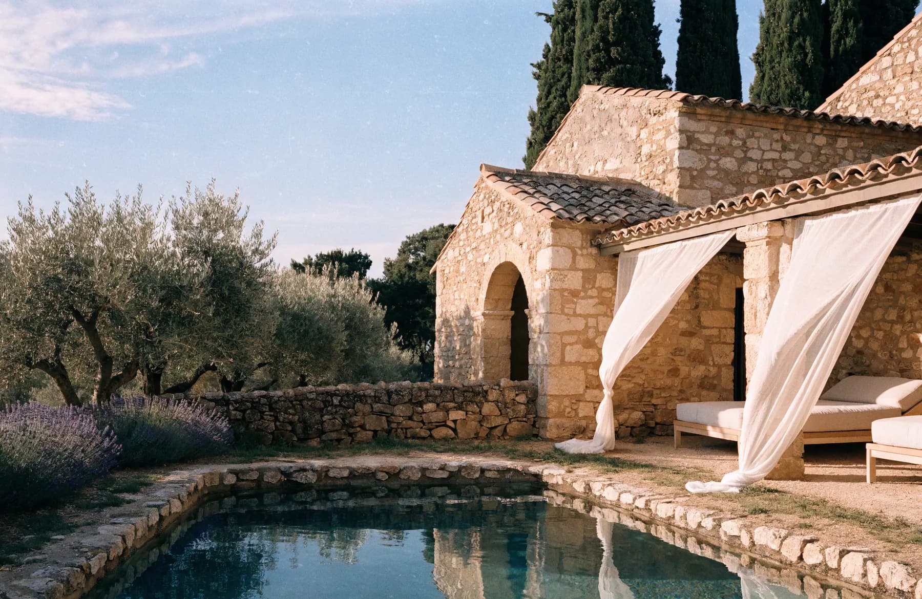 A draped Provençal stone retreat and pool in warm golden light.